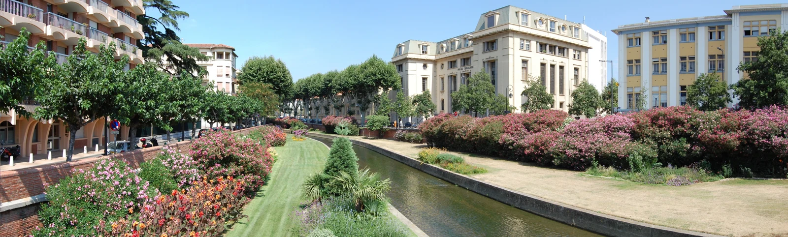 La Basse bordée de jardins fleuris et de bâtiments du centre-ville de Perpignan.