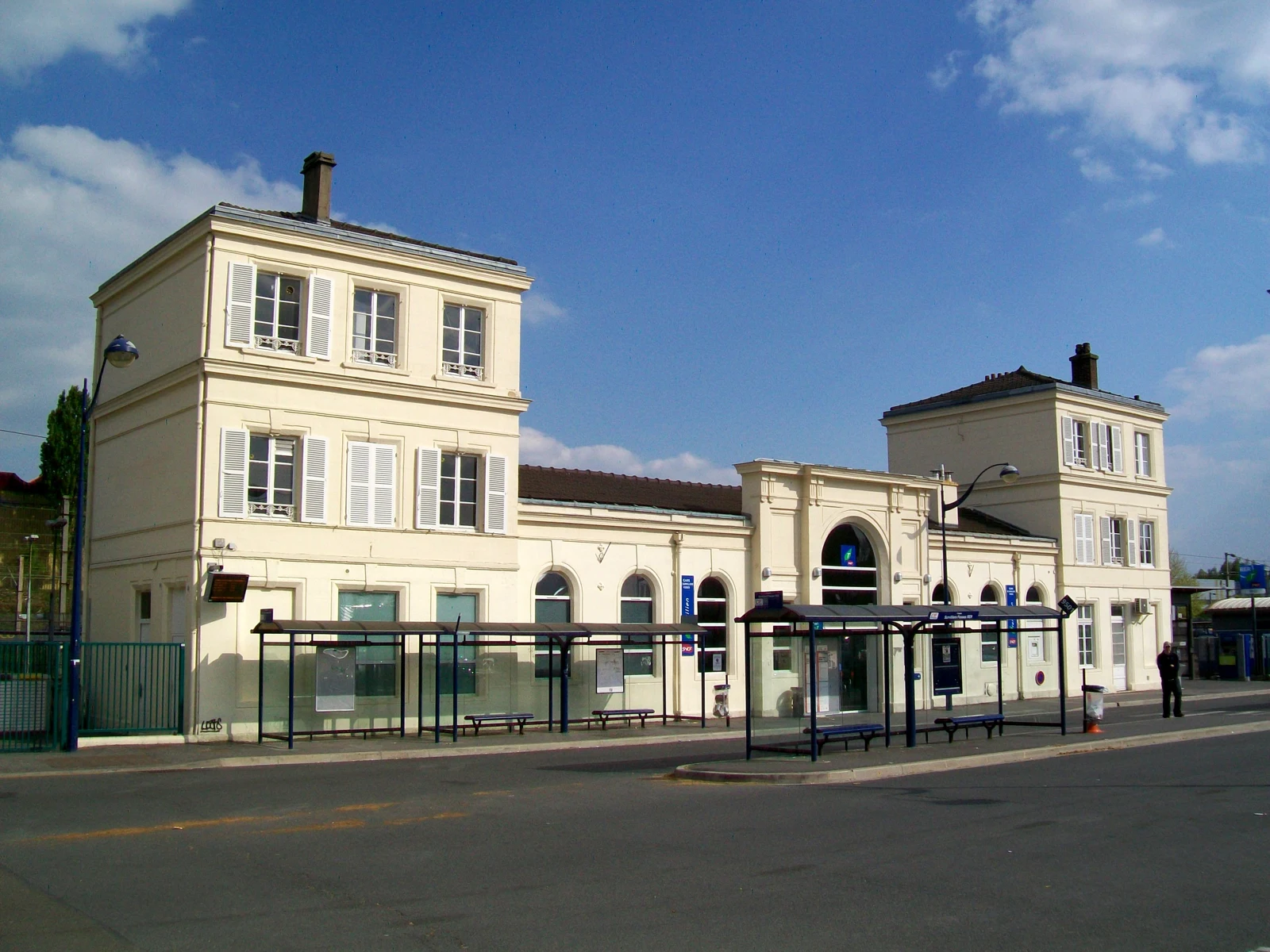 Façade claire de la gare de Survilliers–Fosses, avec ses abris de bus au premier plan.