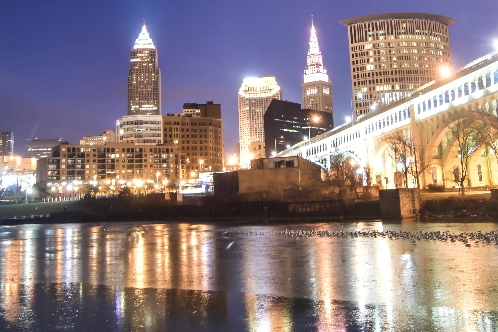 Les immeubles illuminés de Cleveland et un pont, avec leurs reflets sur l’eau au premier plan.