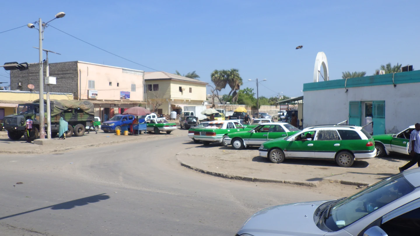 Une rue de Djibouti avec des taxis verts et blancs devant des bâtiments bas.