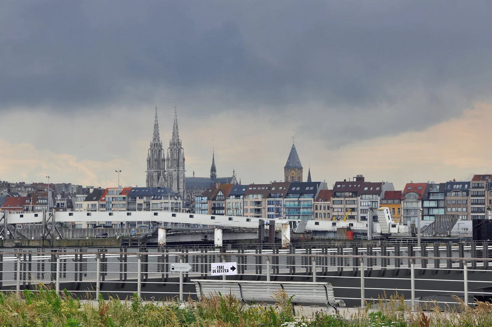 Vue d’Ostende depuis le port, avec les deux flèches de l’église et les immeubles sous un ciel nuageux.