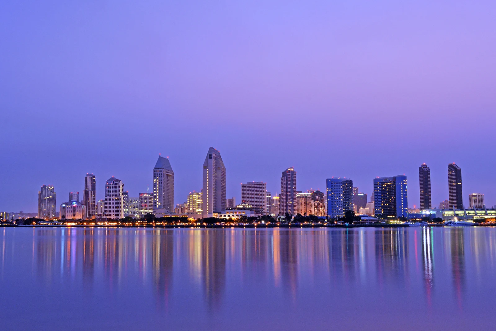 Les immeubles du centre de San Diego et leurs lumières se reflètent dans la baie sous un ciel mauve à l’aube.