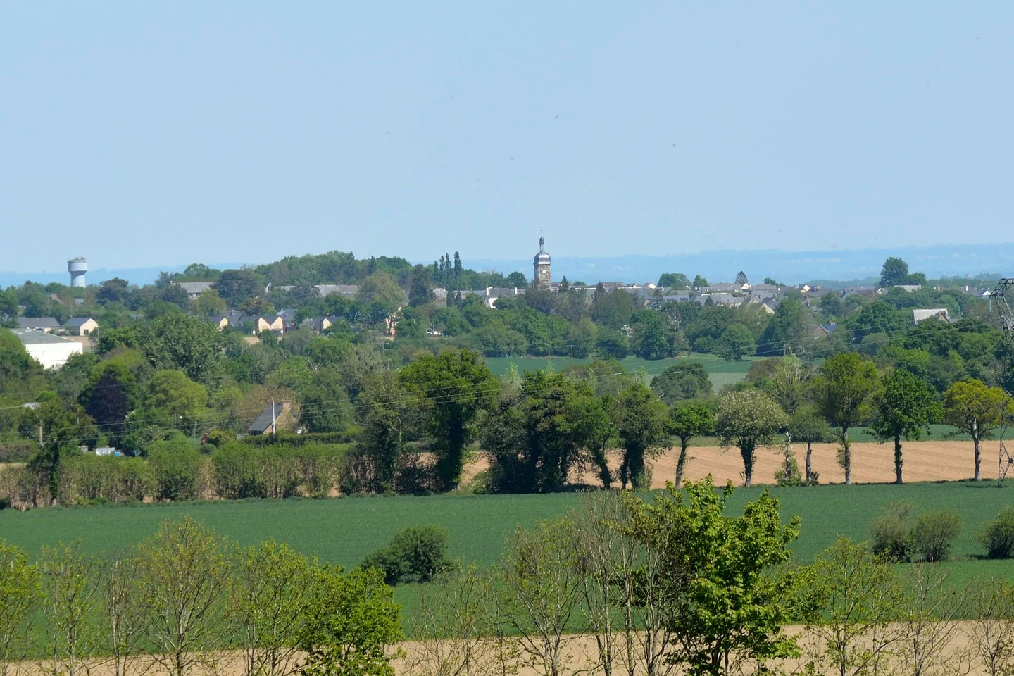 Vue de Pleine-Fougères au-delà des champs et des haies, avec le clocher du bourg au centre.