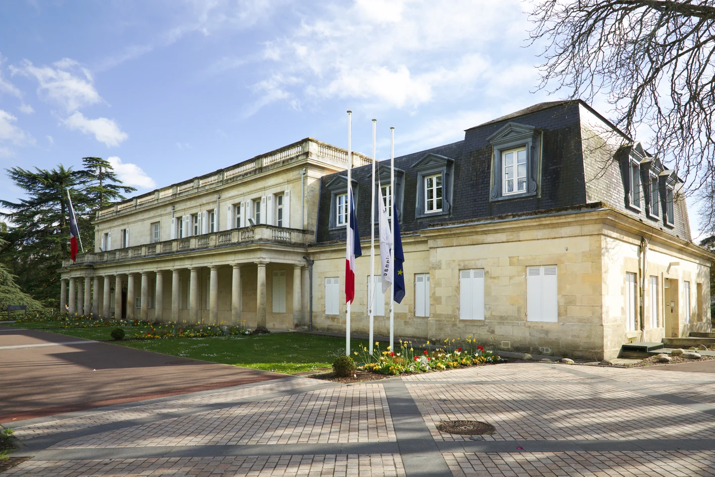 Façade en pierre de la mairie de Mérignac, avec ses colonnes et les drapeaux devant le bâtiment.