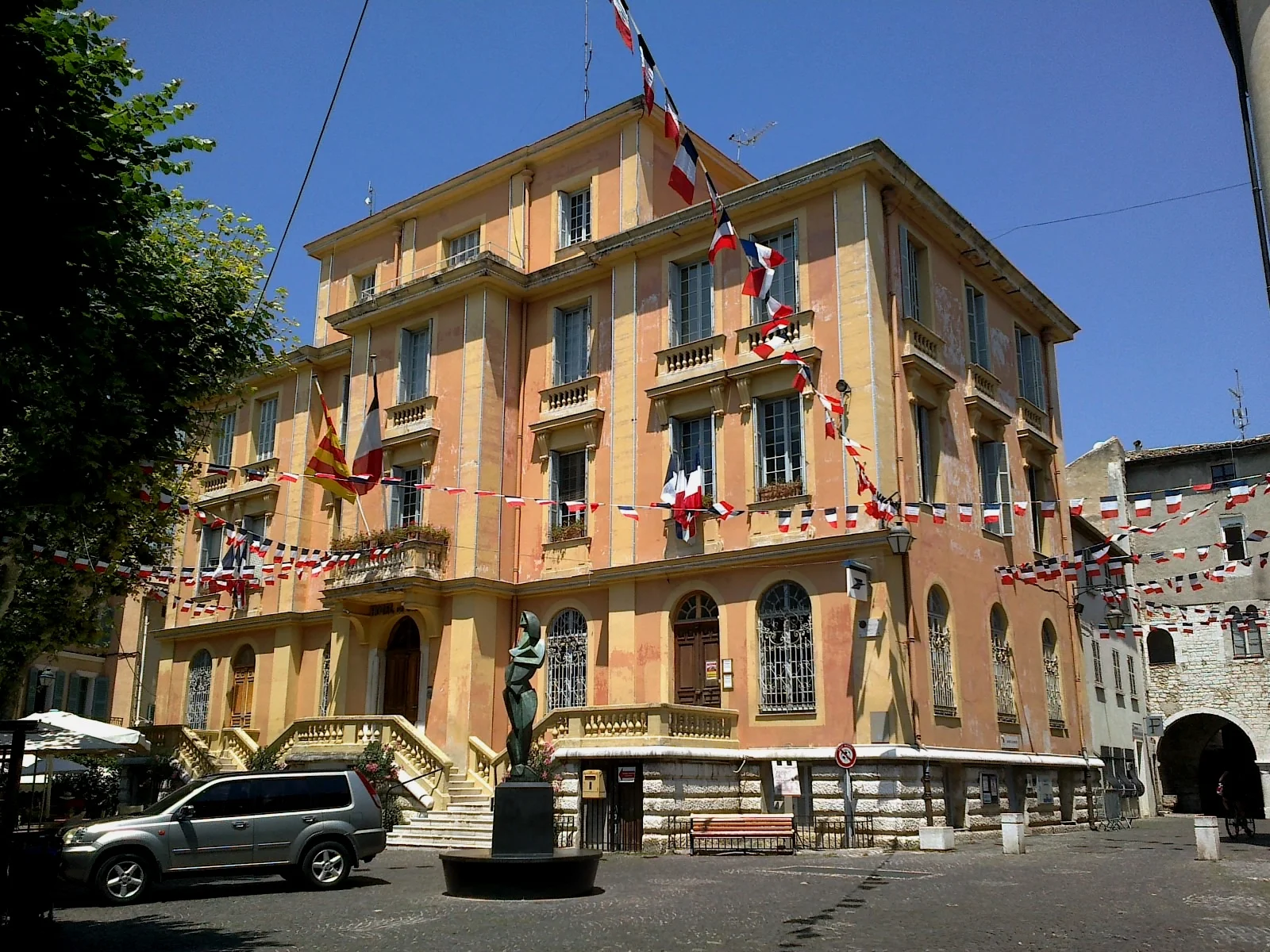 La mairie de Vence, bâtiment ocre orné de drapeaux tricolores, sous un ciel bleu.