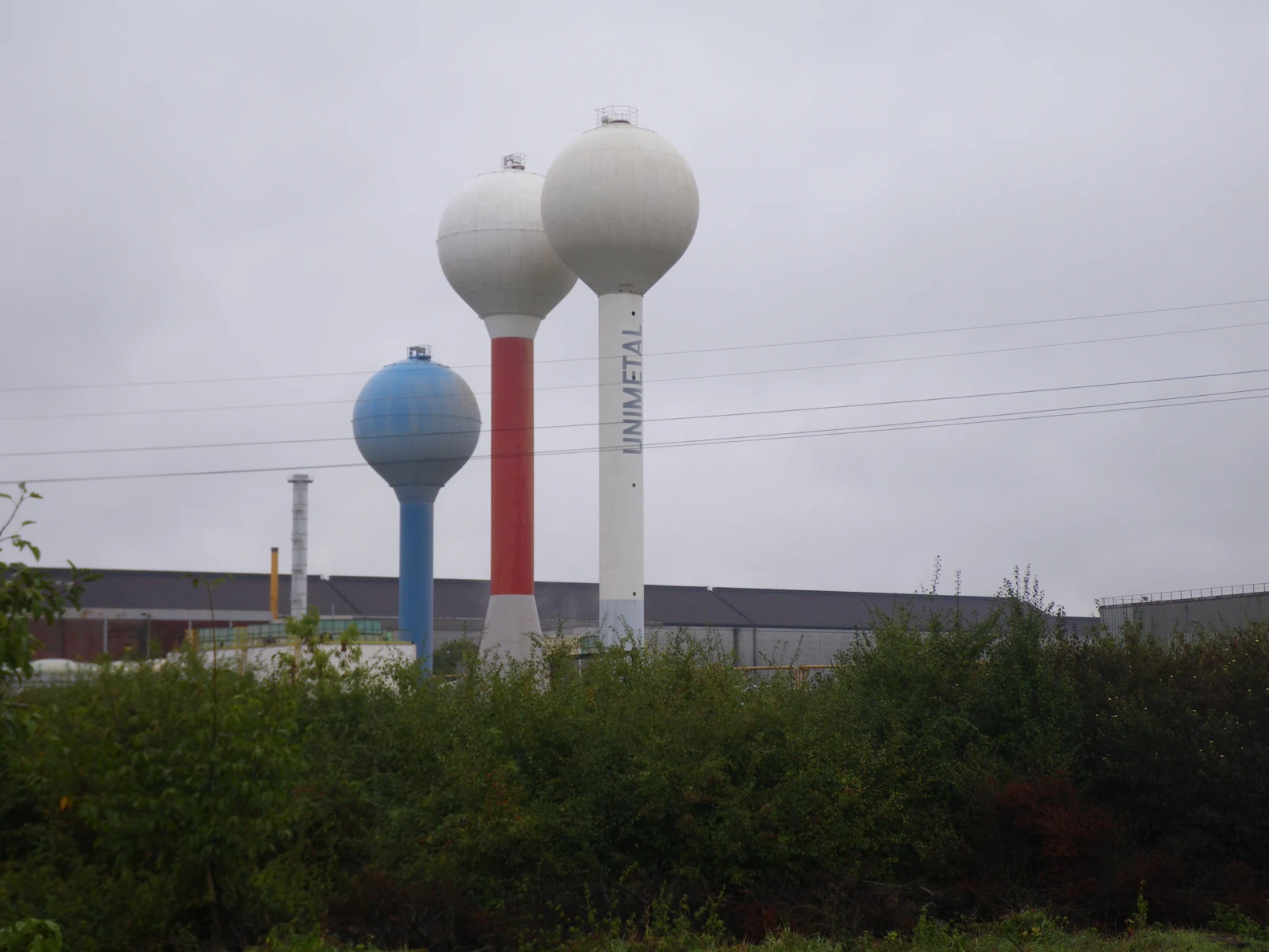 Trois châteaux d’eau industriels à Amnéville, derrière une végétation dense, sous un ciel couvert.