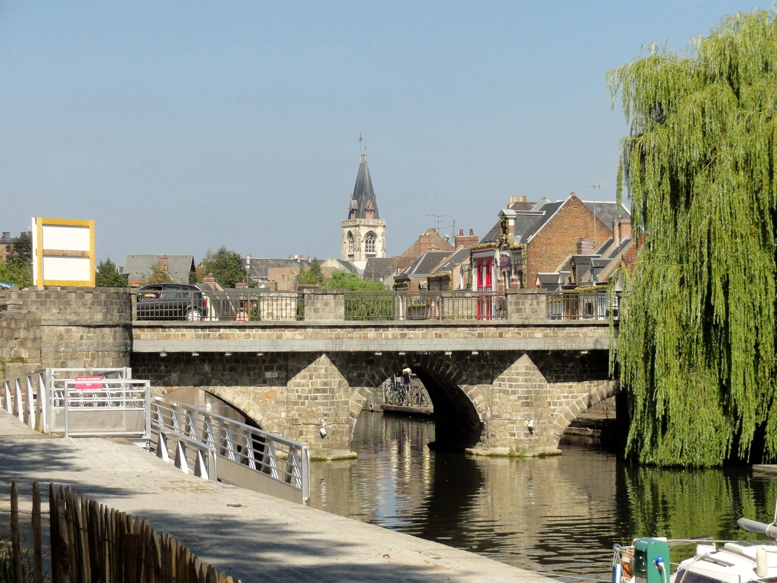 Pont de pierre sur un bras de la Somme à Amiens, avec le clocher de Saint-Leu et un saule en arrière-plan.