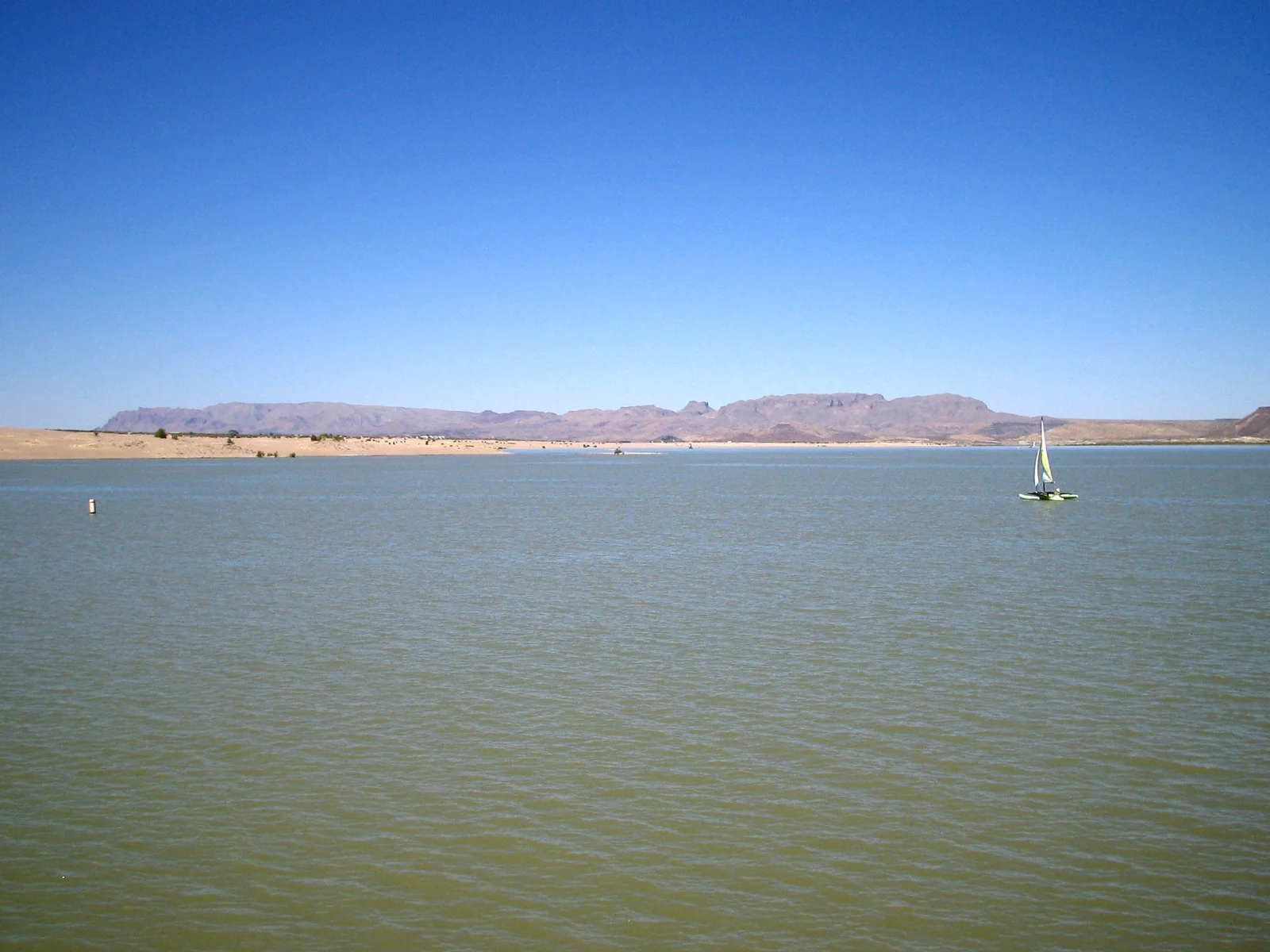 Vue de contexte du lac Elephant Butte : étendue d’eau, petit voilier et reliefs désertiques sous un ciel bleu.