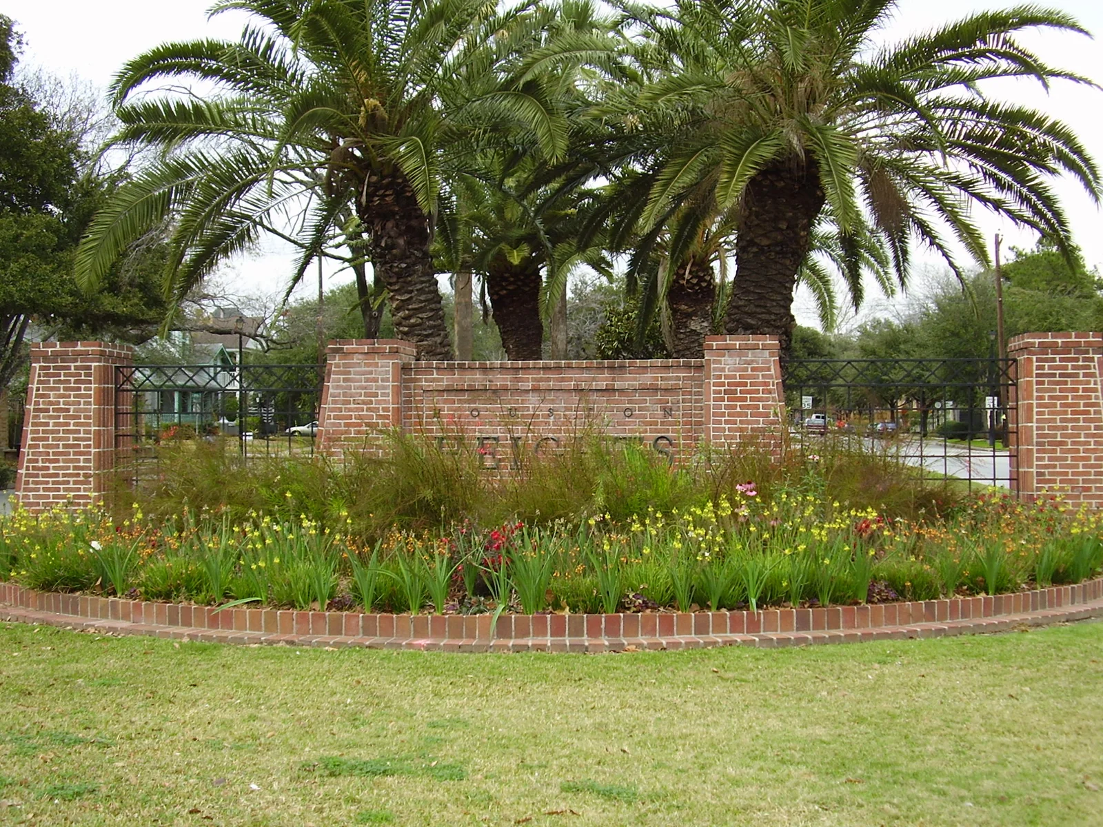 Vue de contexte de Houston Heights : panneau en briques entouré de palmiers et de végétation, à Houston.