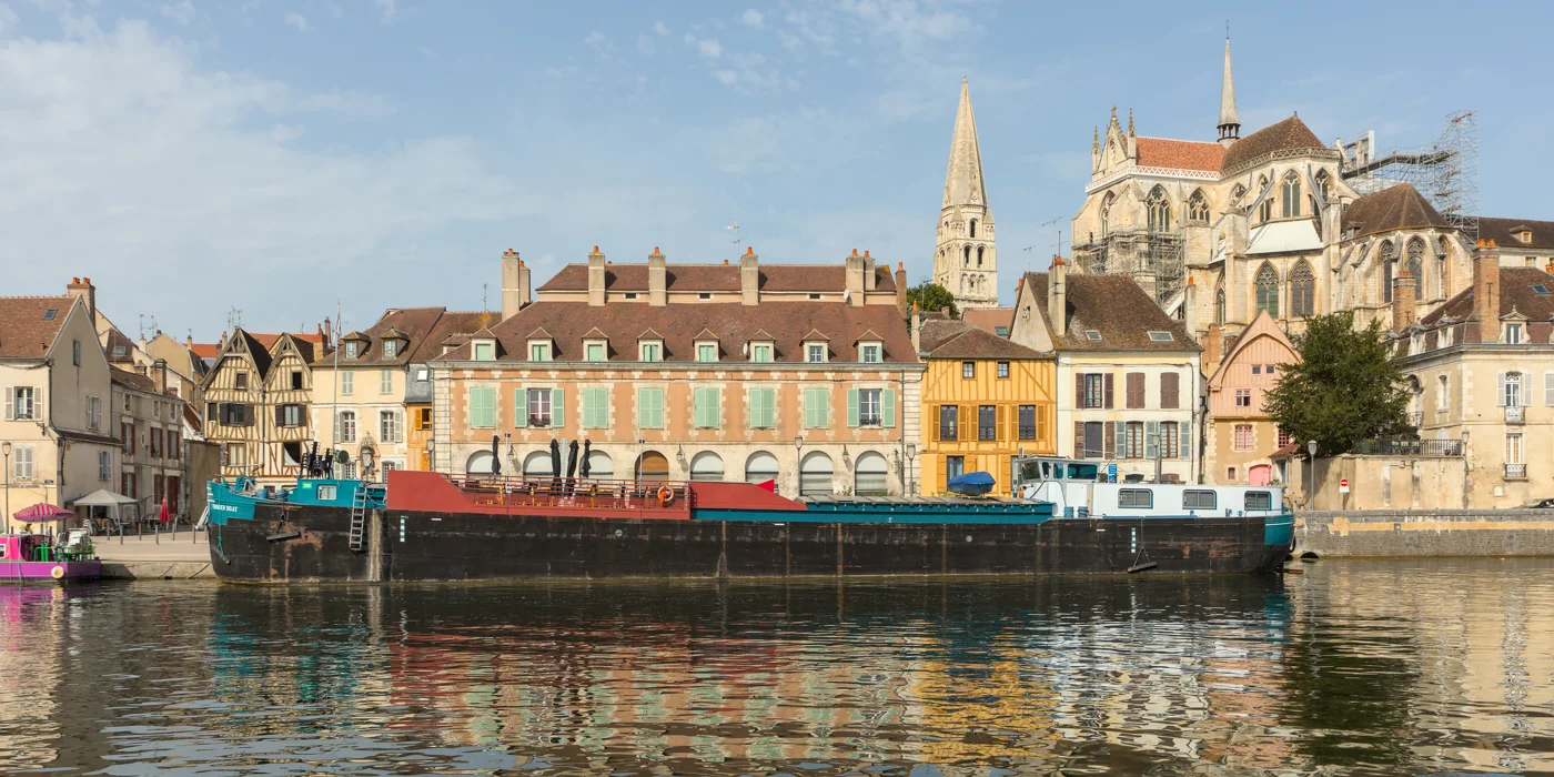 Les façades de la vieille ville d’Auxerre et l’abbaye Saint-Germain derrière une péniche amarrée sur l’Yonne.