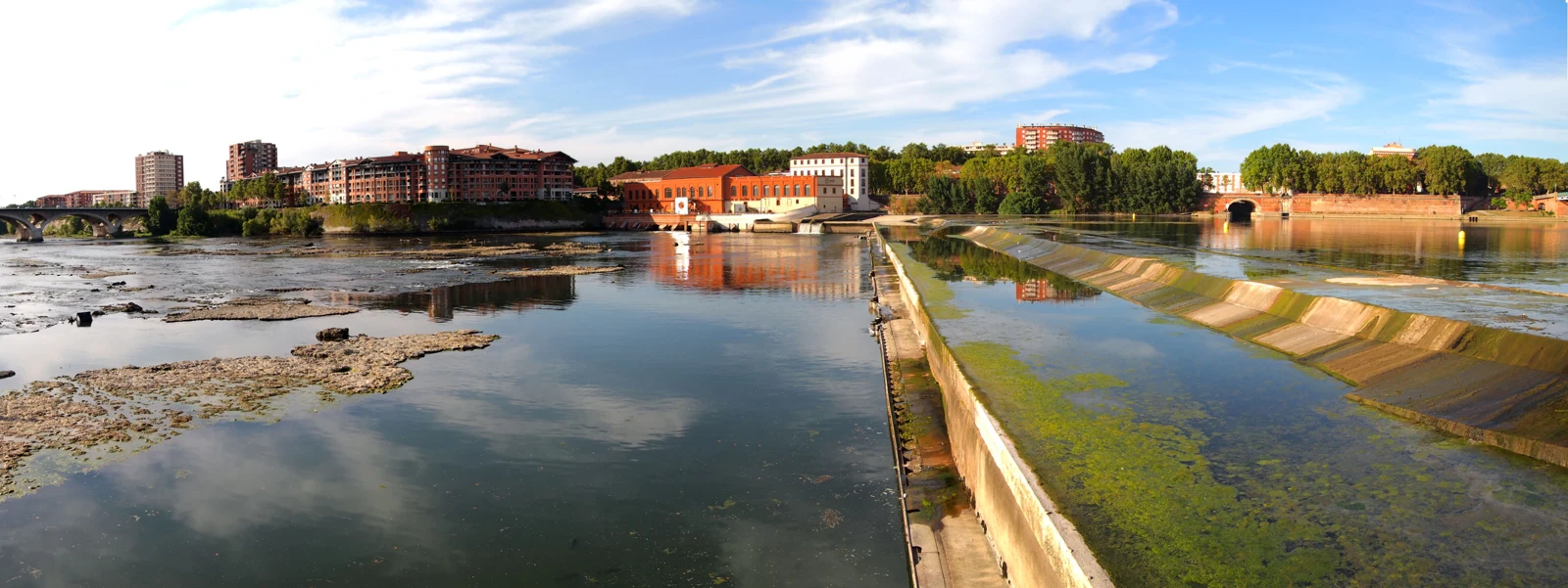 Panorama de la Garonne à Toulouse, avec les bâtiments de briques sur la rive et le fleuve au premier plan.