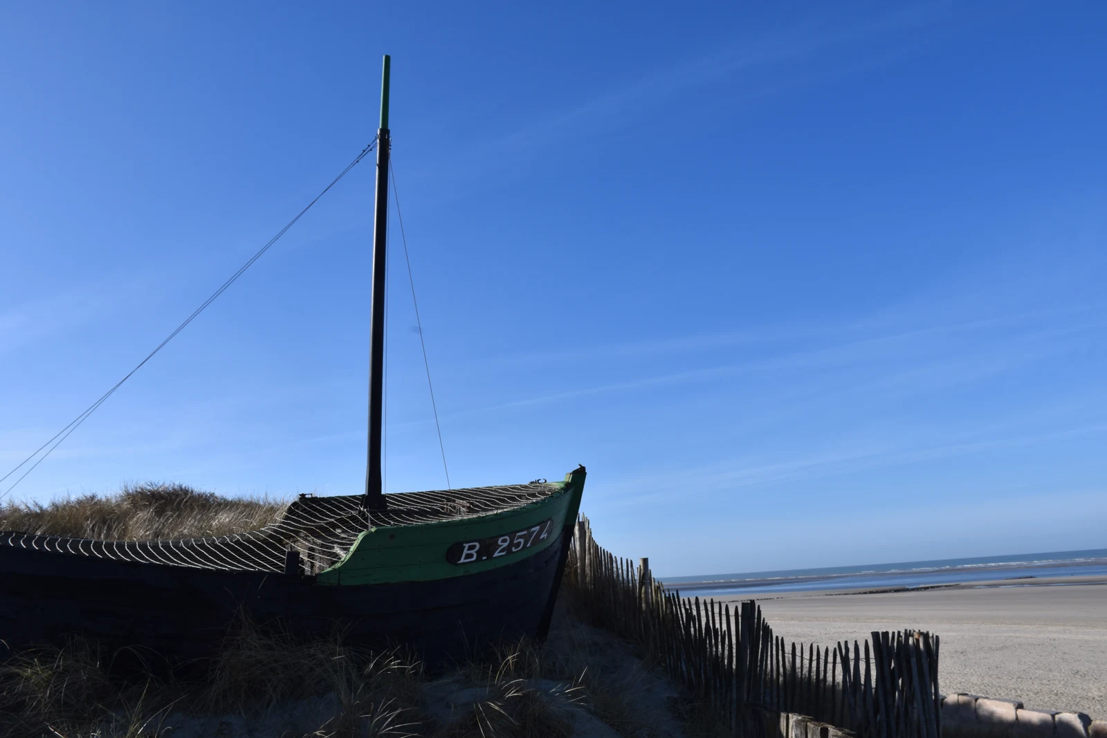 La plage de Berck et la mer, avec une embarcation traditionnelle et une clôture de bois au premier plan.