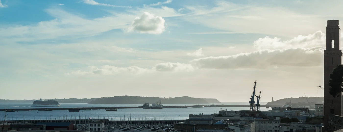 Vue panoramique de la rade de Brest, avec des bateaux, des grues et le port au premier plan.