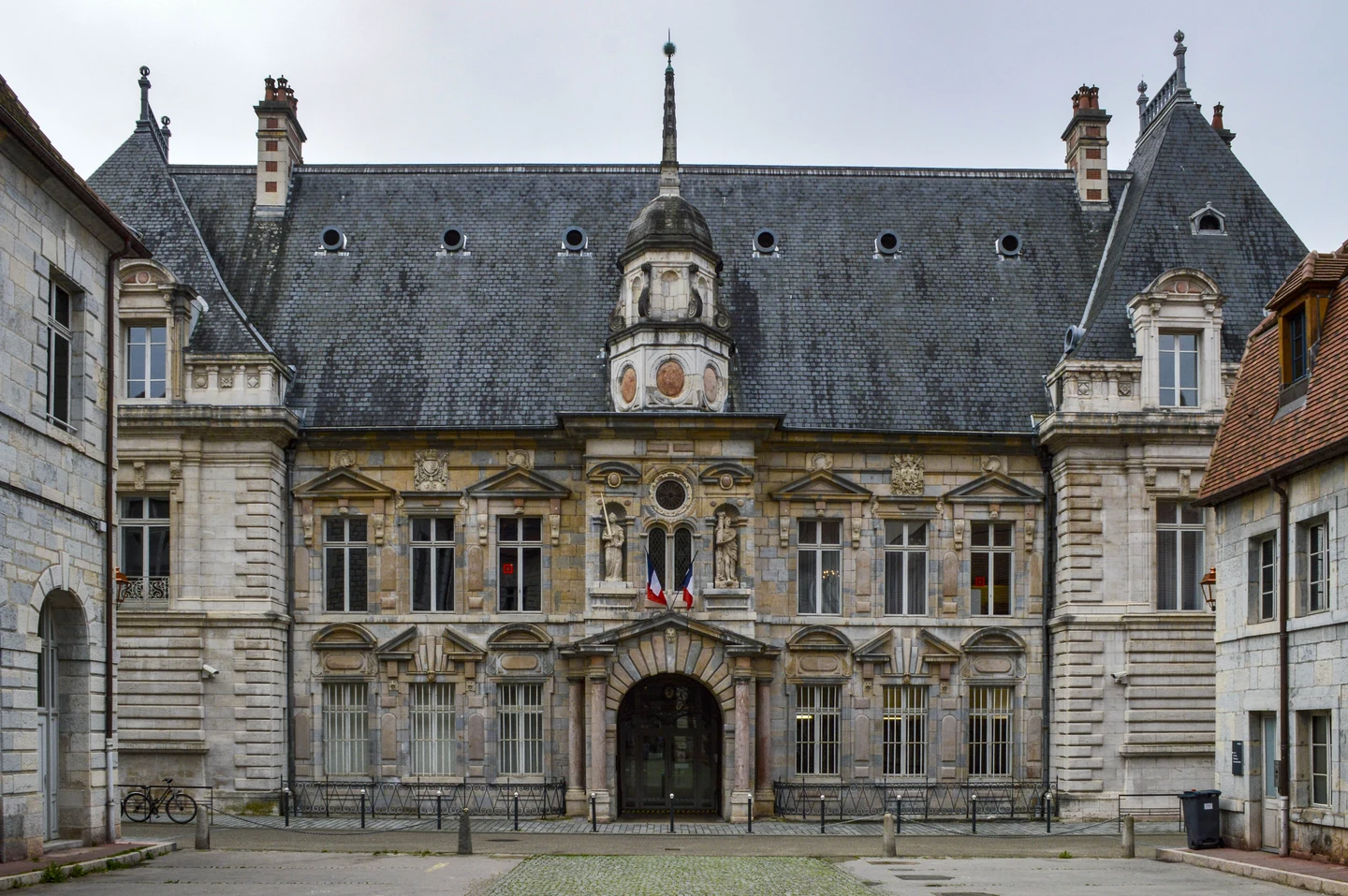 Façade en pierre du palais de justice de Besançon, avec deux drapeaux français au-dessus de l’entrée.