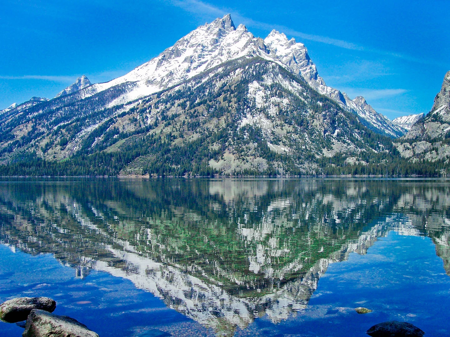 Sommets enneigés des Tetons se reflétant dans un lac sous un ciel bleu.