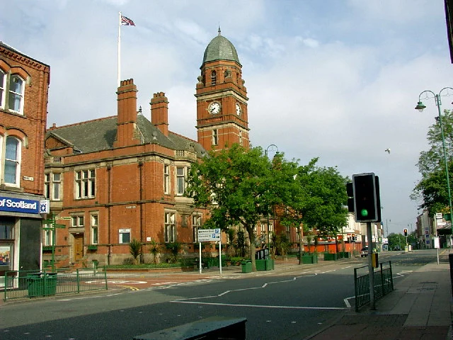 Hôtel de ville en briques rouges et tour de l’horloge de Hyde, dans le Grand Manchester, au bord d’une rue.