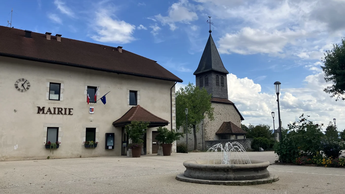 Mairie et clocher de l’église de Prévessin-Moëns, avec une fontaine au premier plan.
