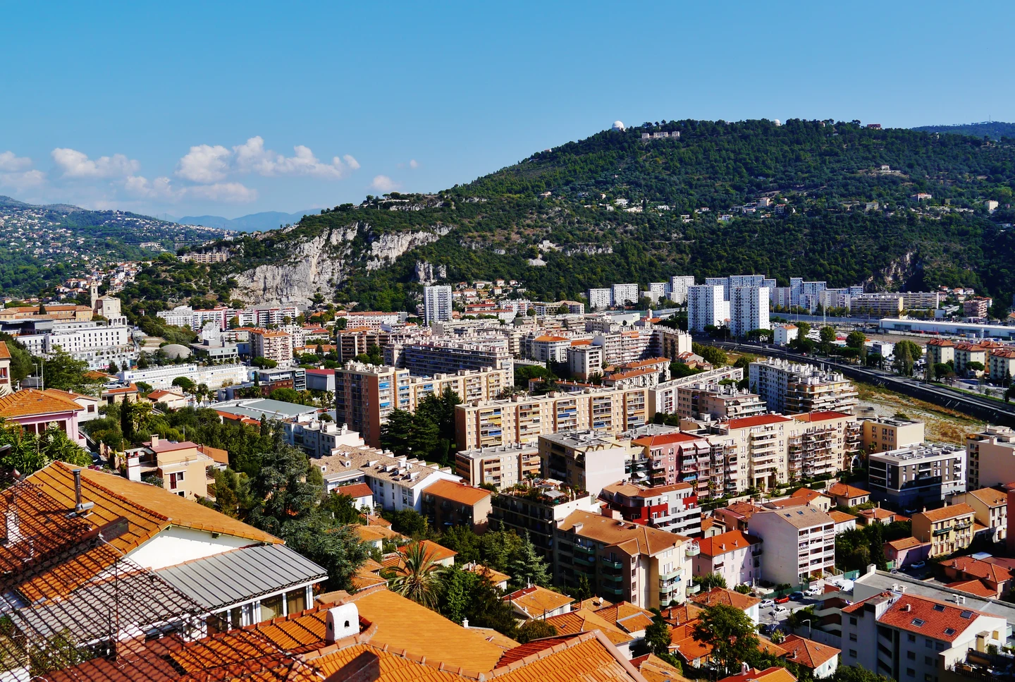 Toits et immeubles de Nice devant une colline boisée, vus depuis Cimiez.