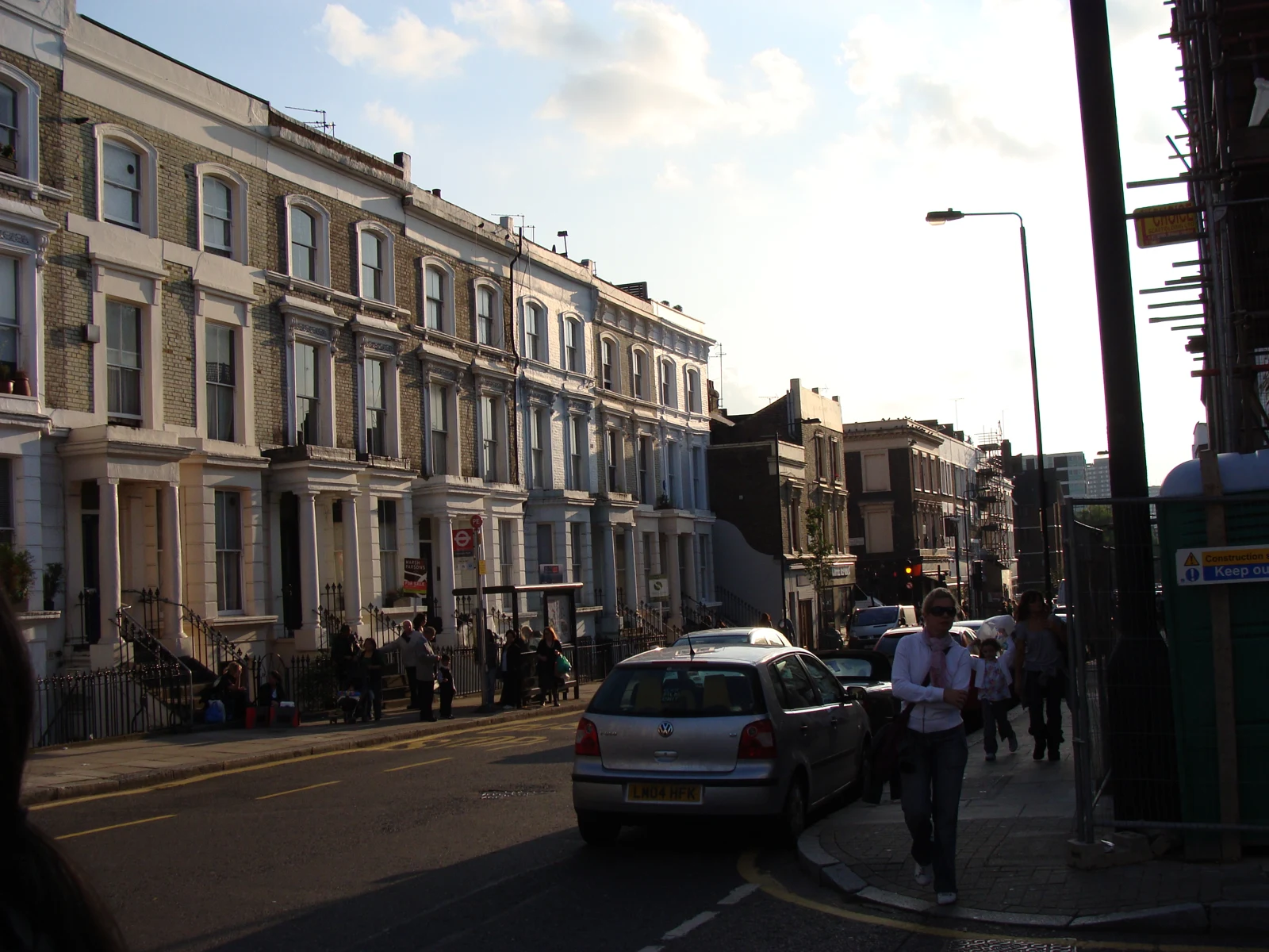 Maisons mitoyennes en briques et façades blanches le long de Westbourne Park Road, à Notting Hill, avec des voitures et des passants.