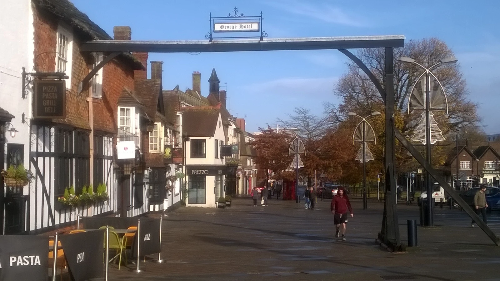 Rue commerçante de Crawley bordée de bâtiments anciens, avec une enseigne George Hotel suspendue au-dessus du trottoir et quelques passants.
