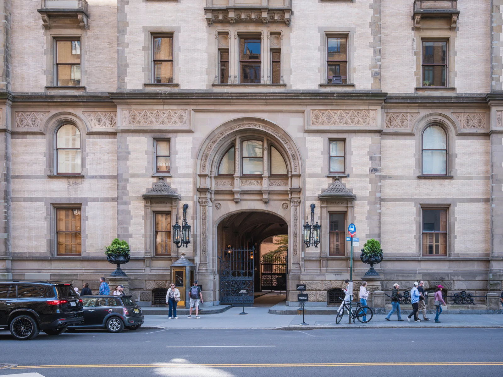 Le porche voûté du Dakota au centre d’une façade de briques claires, avec des passants sur le trottoir de West 72nd Street.