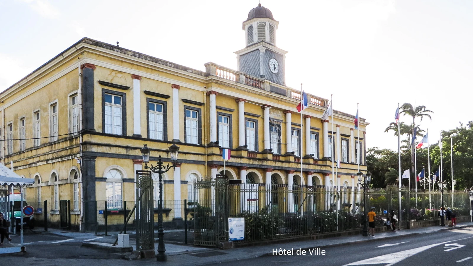 Façade jaune de l’ancien hôtel de ville de Saint-Denis de La Réunion, avec son horloge et ses drapeaux.