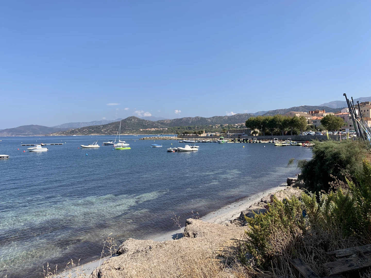 Bateaux dans le port de L’Île-Rousse, entre le rivage rocheux, la ville et les collines corses.