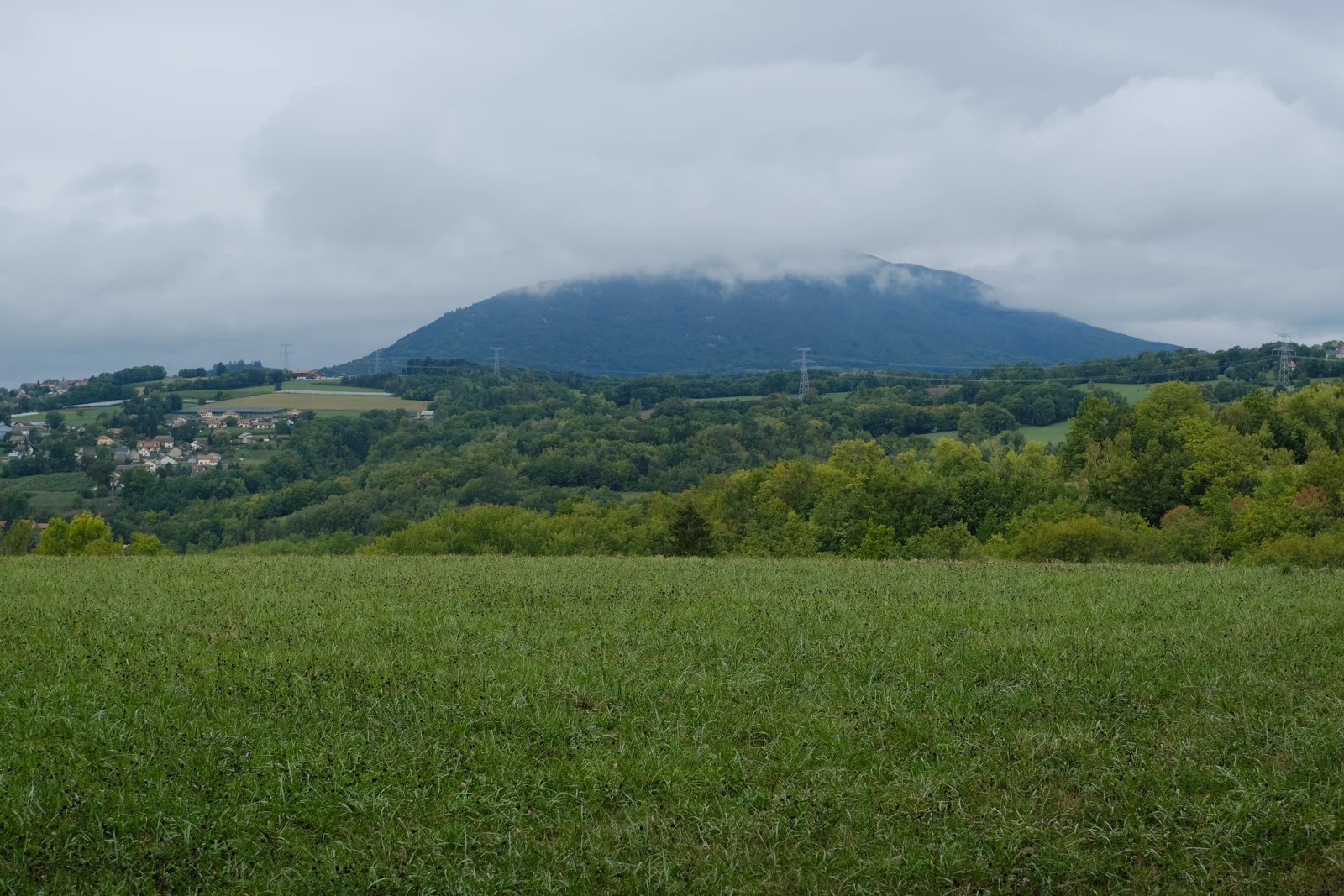 Le massif boisé du Vuache sous un ciel nuageux, au-delà de champs et de villages en Haute-Savoie.