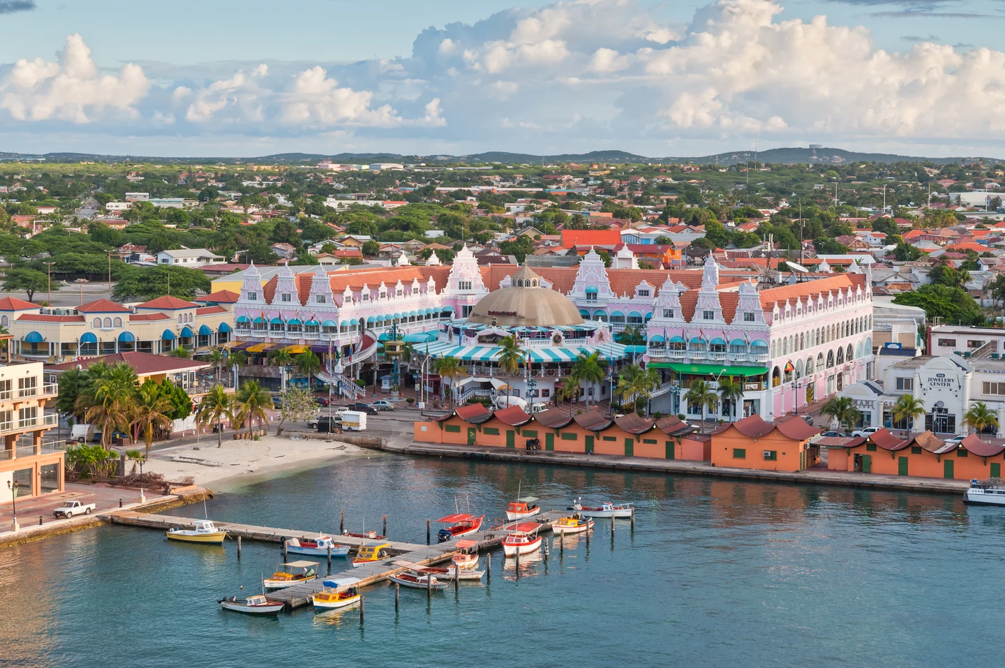Vue d’Oranjestad, à Aruba, avec les façades roses du Royal Plaza Mall et des bateaux au premier plan.