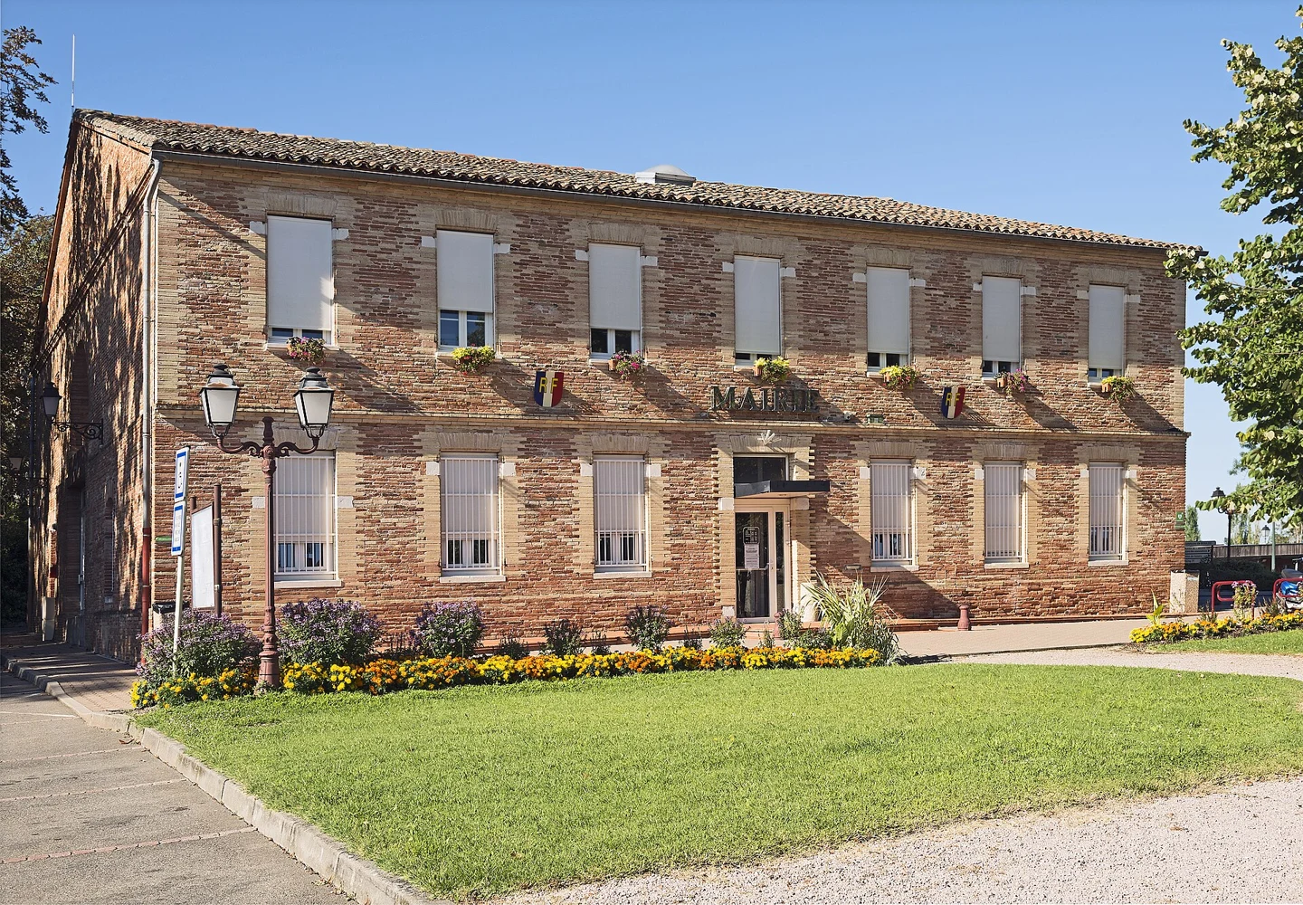 Façade en briques de la mairie de Bouloc, avec un jardin au premier plan.