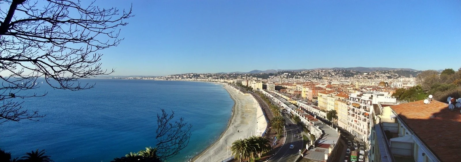 Vue panoramique de Nice, de ses immeubles en bord de mer et de la baie sous un ciel bleu.