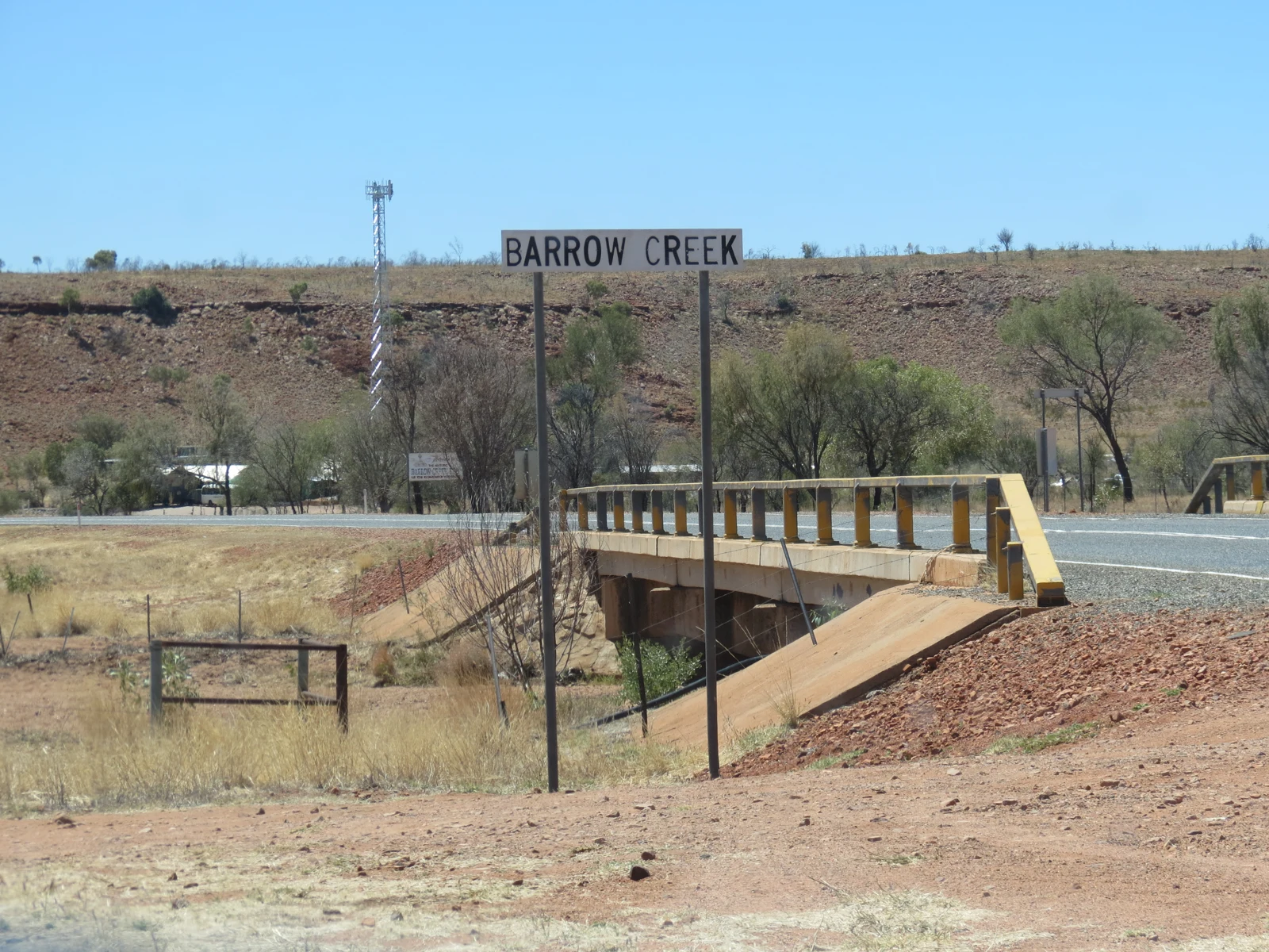 Panneau « Barrow Creek » devant un petit pont routier, dans un paysage sec du Territoire du Nord australien.