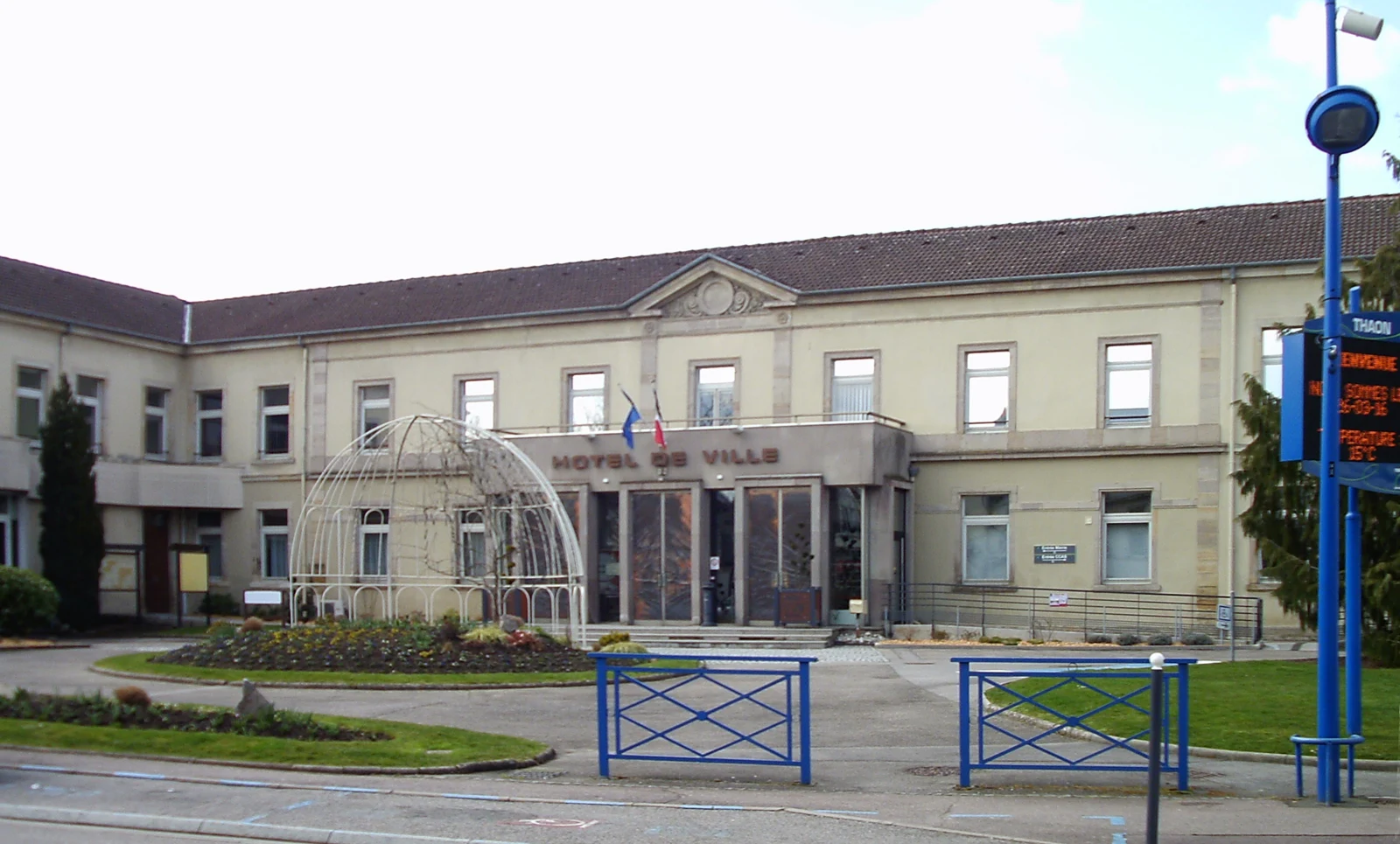 Hôtel de ville de Thaon-les-Vosges, bâtiment clair entouré de rues et d’arbres.