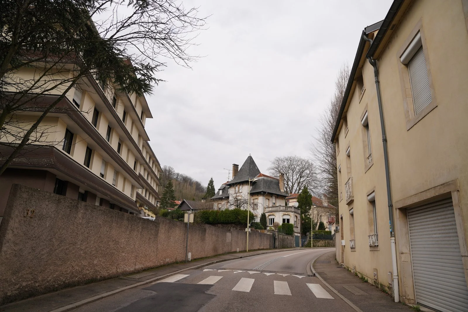 Rue bordée de bâtiments et d’arbres à Maxéville, sous un ciel couvert, sans personne visible.