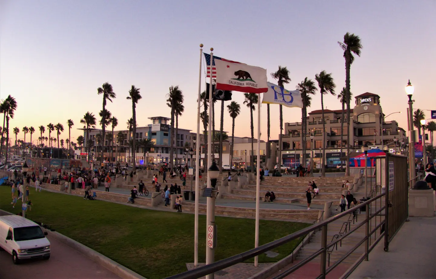 Place du front de mer de Huntington Beach au crépuscule, avec palmiers et drapeaux.
