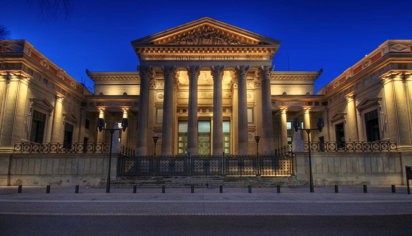 La façade à colonnes du palais de justice de Nîmes, éclairée à la tombée de la nuit.
