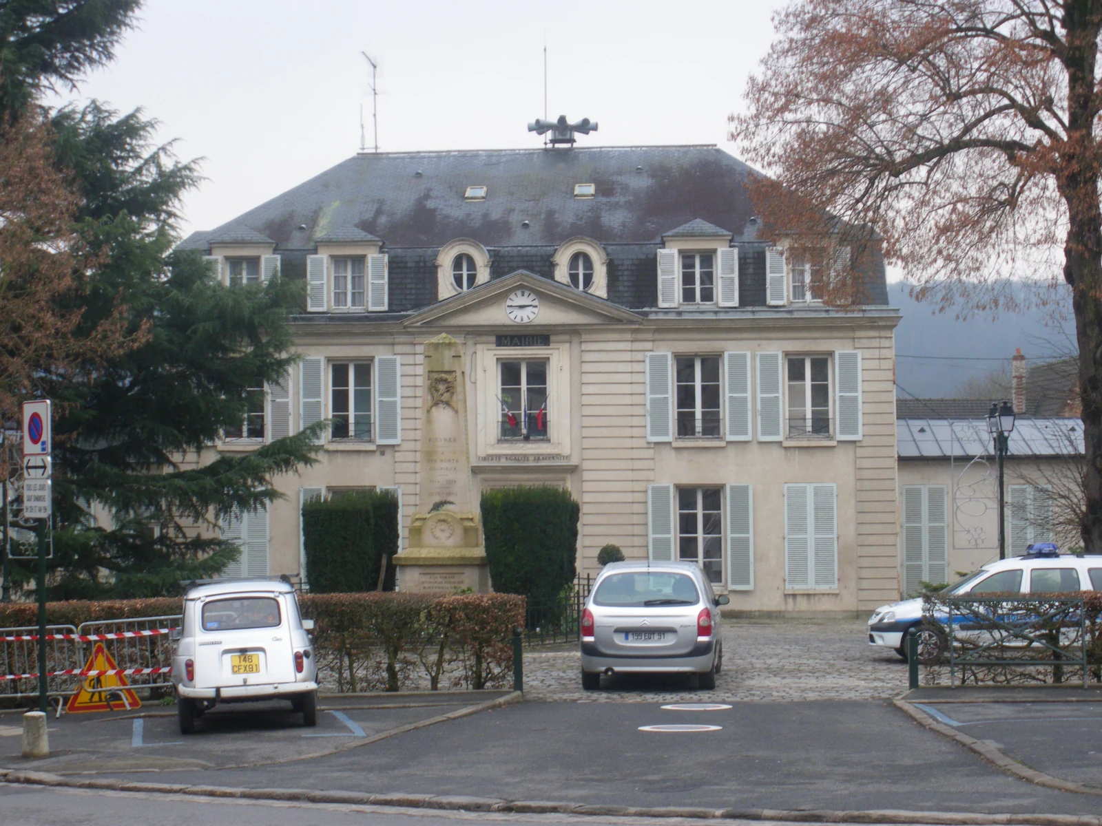 Façade de la mairie de Bièvres, dans l’Essonne, avec un monument aux morts et des voitures au premier plan.