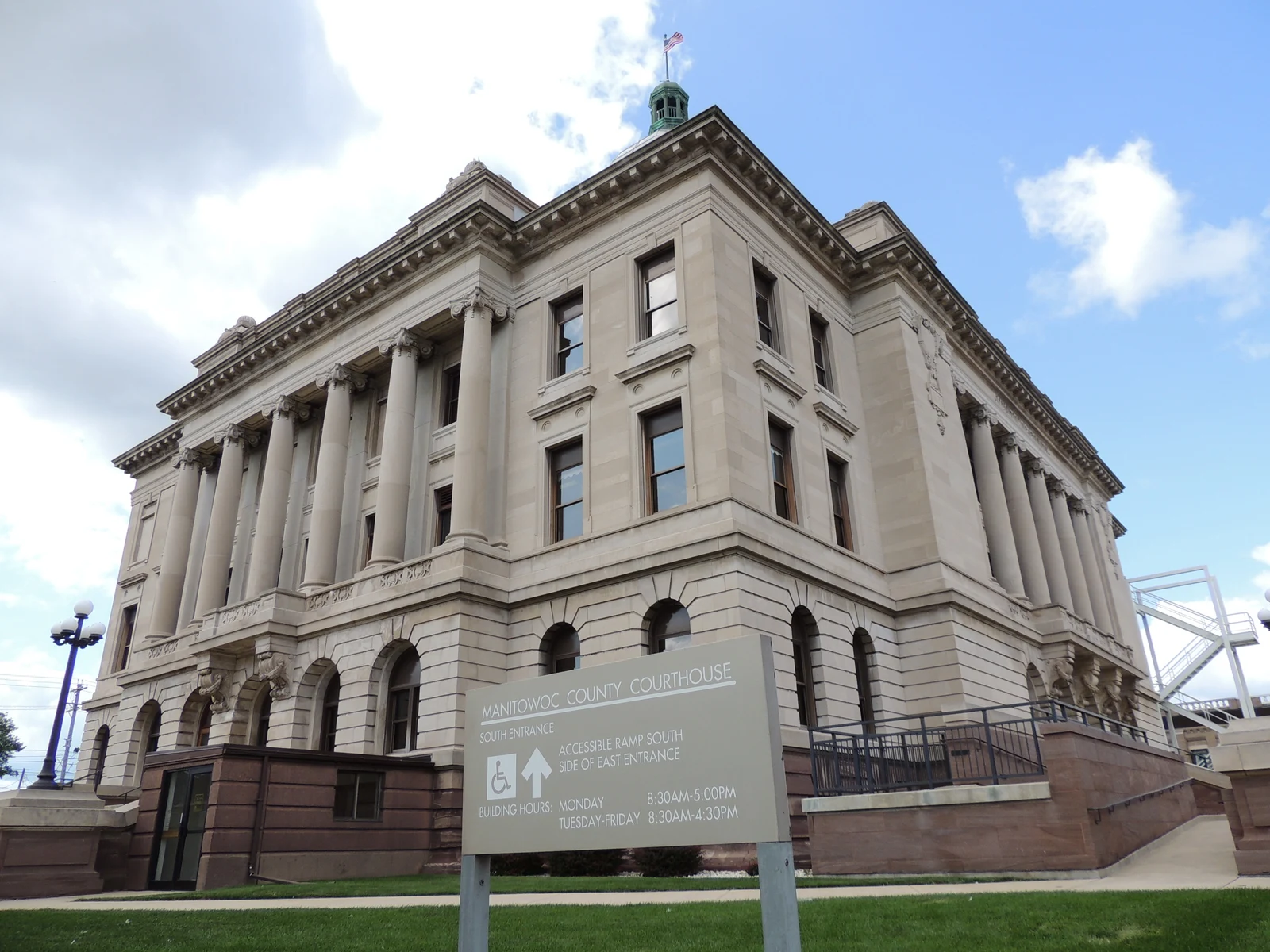 Le palais de justice du comté de Manitowoc, bâtiment de pierre à colonnes, avec son panneau d’entrée au premier plan.