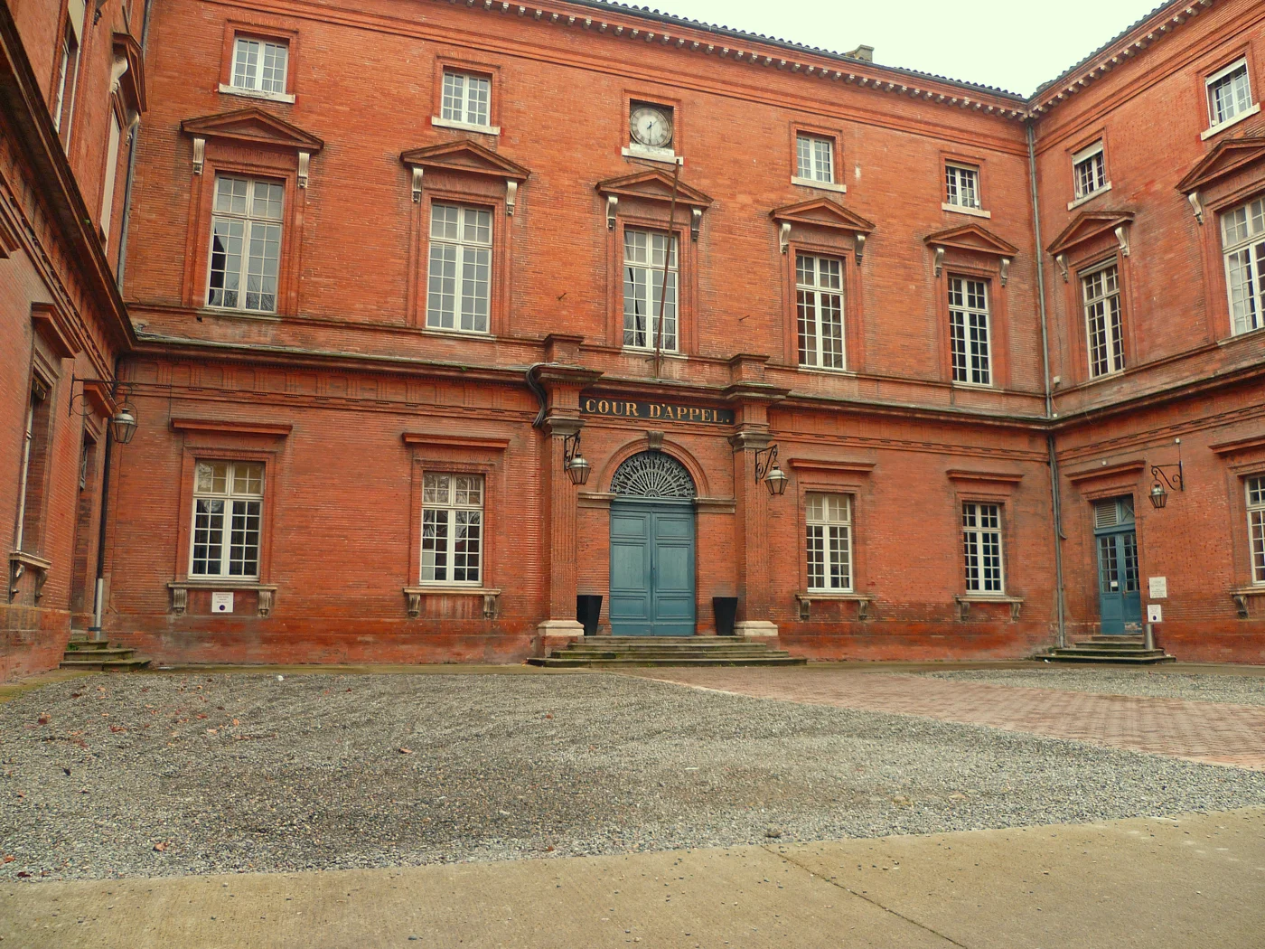 Façade en briques de la cour d’appel de Toulouse, avec une porte bleue et une horloge.