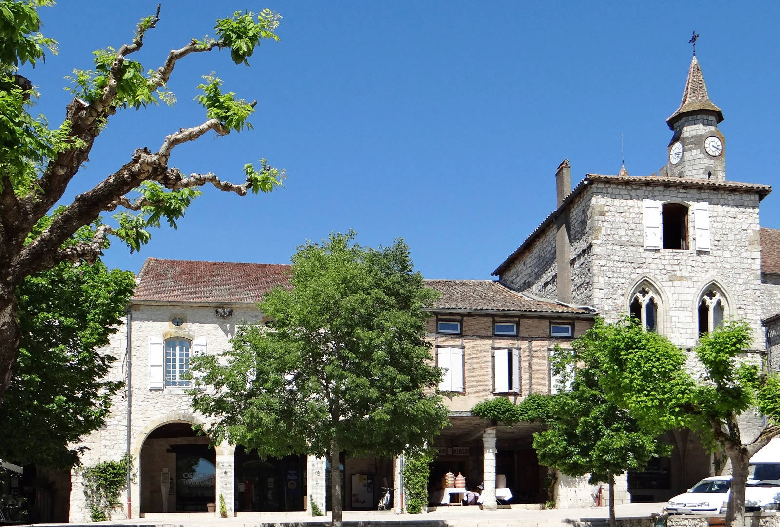 Façades de pierre et arcades bordées d’arbres sur la place des Arcades à Monflanquin.