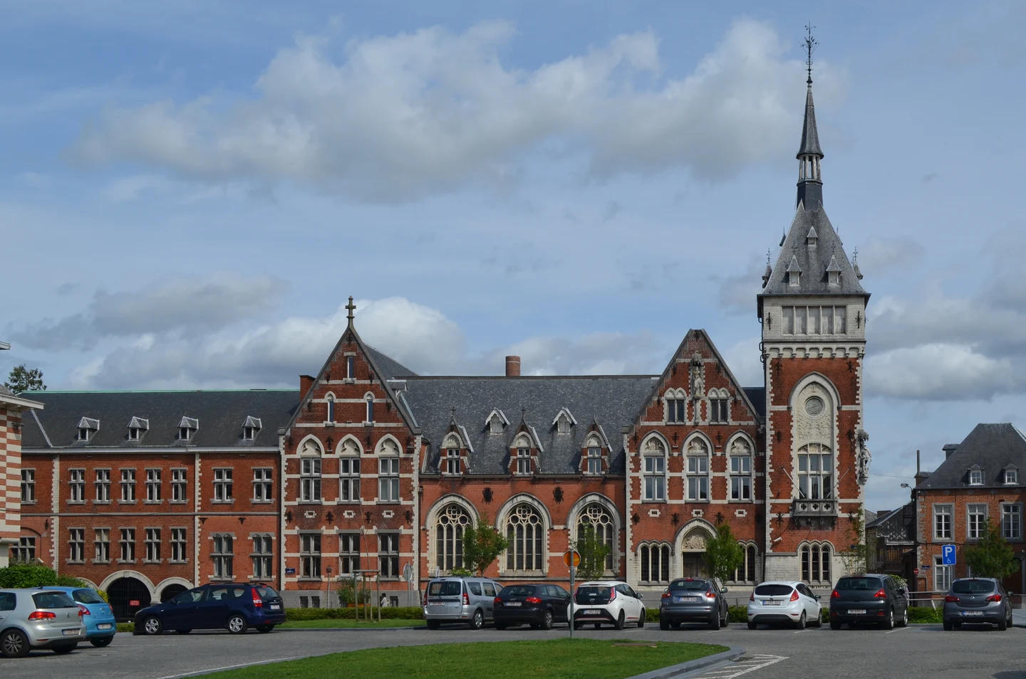Palais de justice en briques rouges de Nivelles, avec sa haute tour et des voitures sur la place.